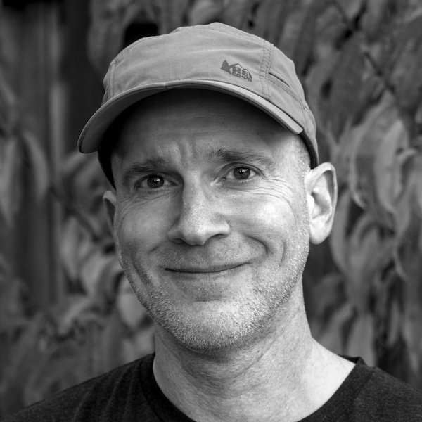 Black and white portrait of a middle-aged white guy wearing a ballcap. Presumably Steve Sprang.